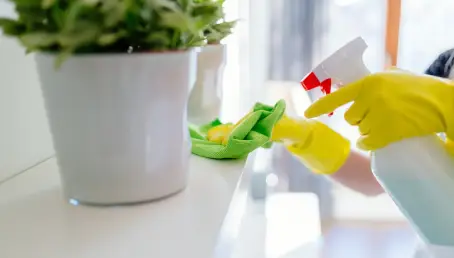 Person in yellow rubber gloves cleaning a cleaning white shelf.
